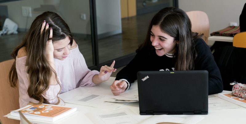 Two spanish girls with computer and papers discussing merrily